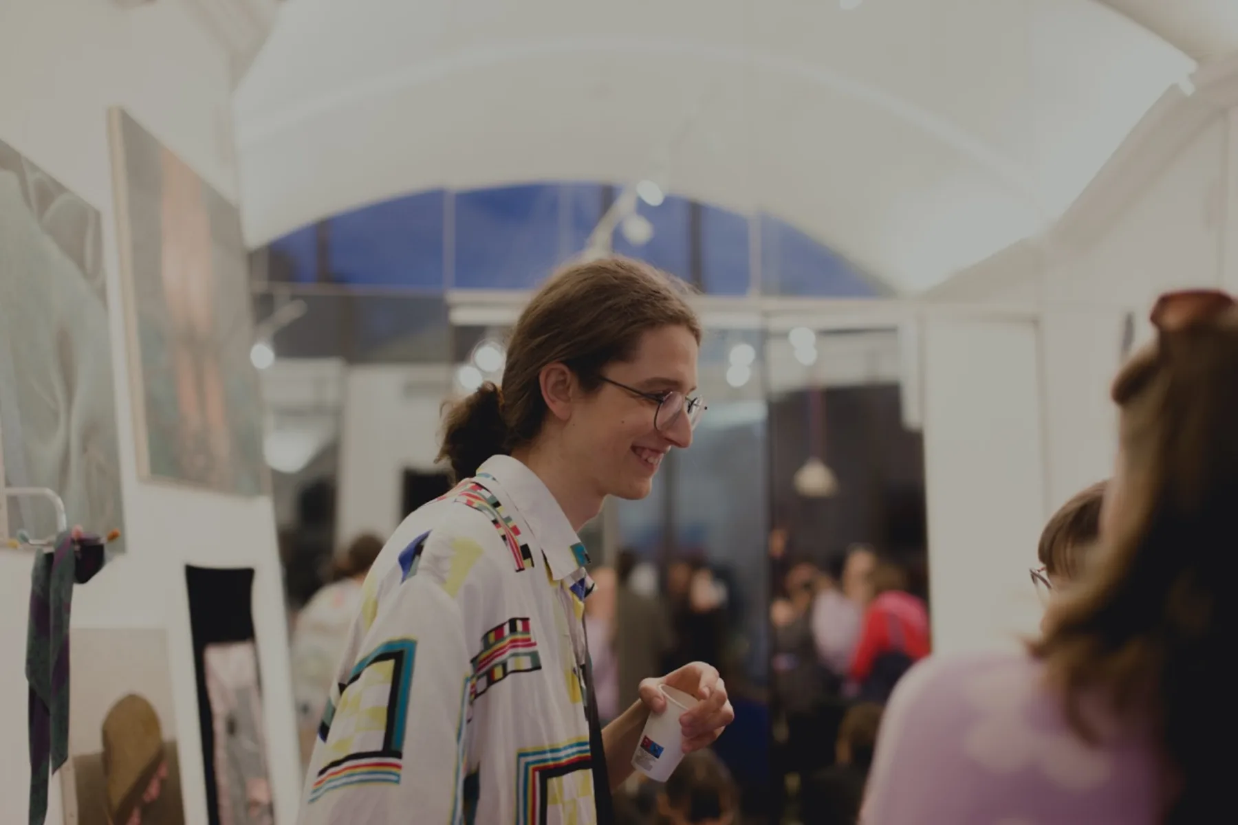 Patryk na wystawie, rozmawia, w tle prace i goście