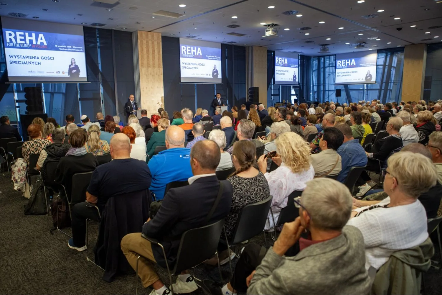 Pełna sala konferencyjna, publiczność na krzesłach słucha prelegentów na scenie, na ekranach napis Wystąpienia gości specjalnych
