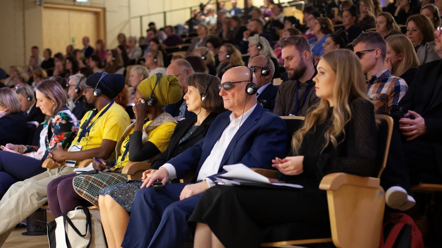 Publiczność na widowni konferencji, wiele osób w słuchawkach do tłumaczenia symultanicznego, uważnie słucha